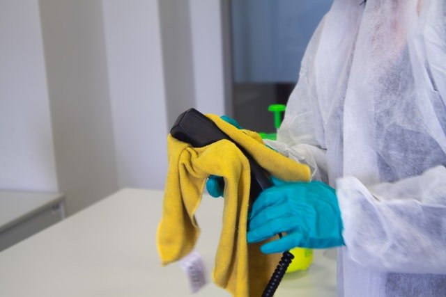 A person with cleaning equipment cleaning a phone. Having the right equipment is one of the benefits of hiring a cleaning service.