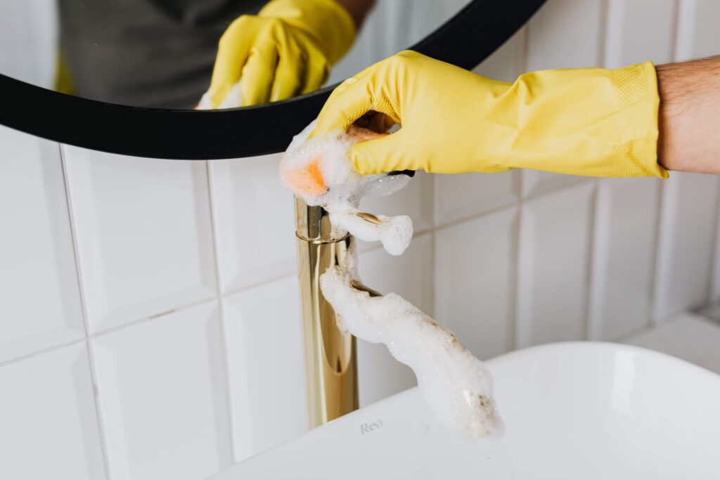 A professional cleaner in yellow gloves, cleaning a tap in the bathroom