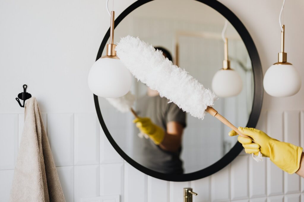 A person wearing yellow gloves, dusting lighting fixtures in a bathroom