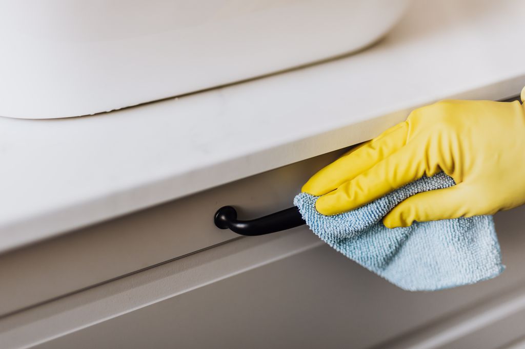 A person cleaning the knobs on the cabinet.