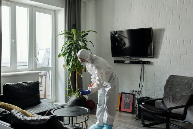 A man in protective gear cleaning a living room table.