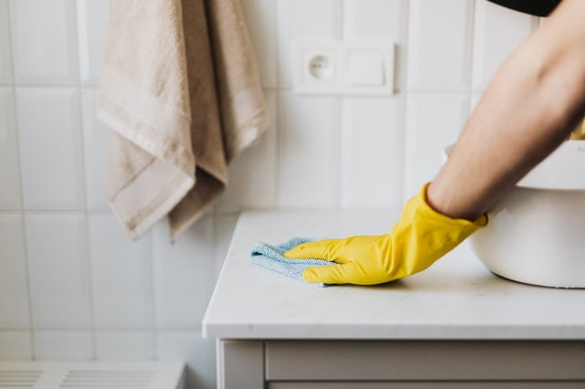 A deep house cleaning service professional wiping a bathroom cabinet.