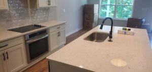 White kitchen cabinets, a stainless-steel sink and a light-colored island countertop.
