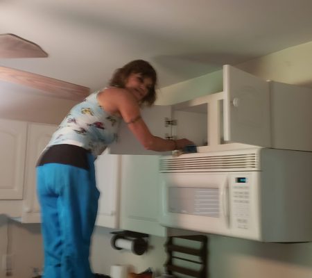 Woman on ladder cleaning inside kitchen cabinets